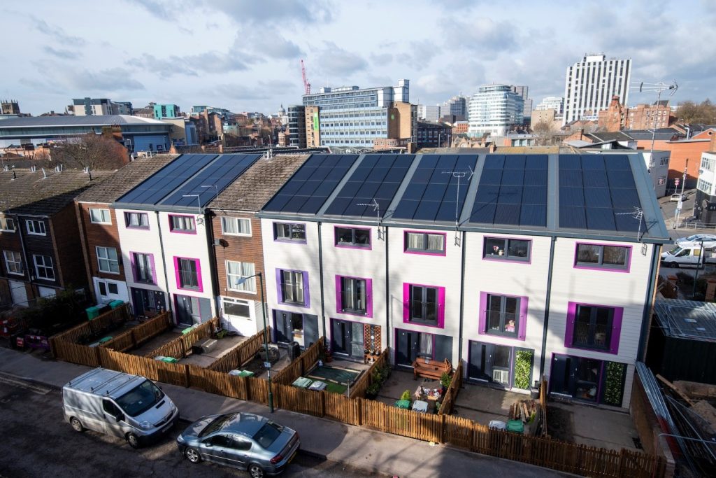 A row of houses with solar panels, back gardens that have been made by fences and cars.