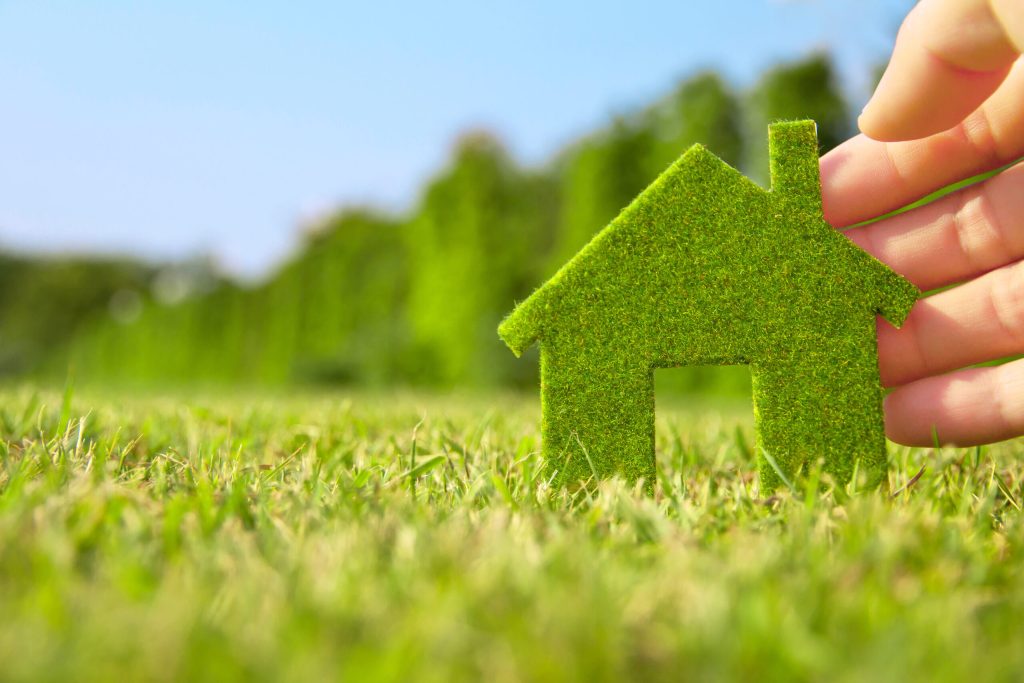 A hand holding a model of a house that has been made from grass in nature.