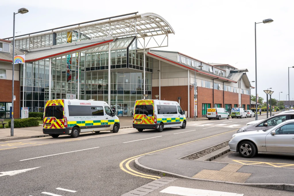 A busy hospital - a perfect example of a building with non-domestic retrofit needs - featuring a modern glass & red-brick exterior and ambulances parked outside