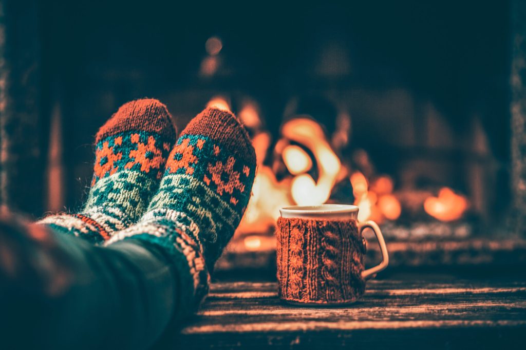 A person's feet in colourful knitted socks next to a mug near a fireplace.