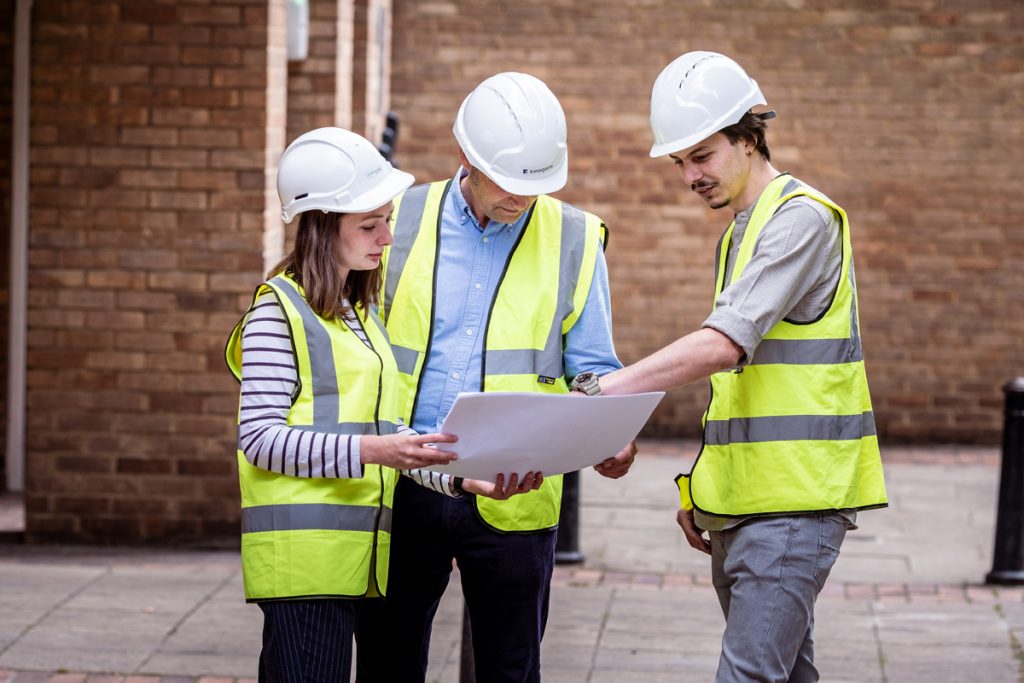 Matt Rock of Keegans - Retrofit Academy Awards 2025 Finalist - Image shows 3 people in white hard hats and high-vis vests looking at plans on A3 size paper.