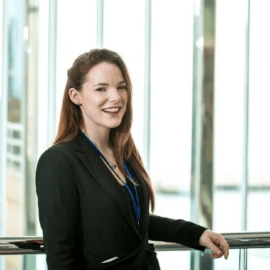 A photo of an individual who has long brown hair and is wearing a black blazer with a black top.