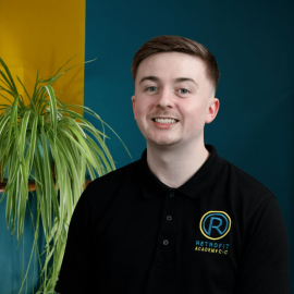 An individual called Charlie Hayes is wearing a Retrofit branded polo whilst posing next to a blue and yellow wall and a plant.