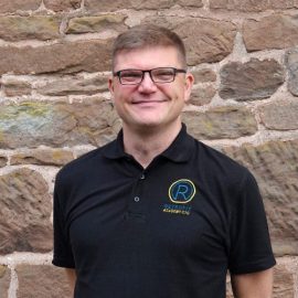 David Pierpoint is wearing a black Retrofit polo t-shirt and is standing in front of a brick wall.