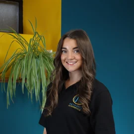 An individual called Katie Felton is posing in front of a yellow and blue wall next to a plant, whilst wearing a black Retrofit Academy branded polo shirt.