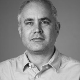 A black and white photo of Richard Fitton, who has short grey hair and is wearing a shirt.