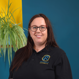 An individual who was long brown hair is wearing a black branded Retrofit polo and is posing in front of a blue wall.